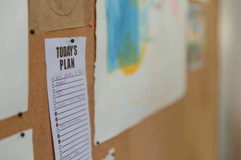 Close-up of a corkboard with a to-do list and colorful artwork in an office setting.